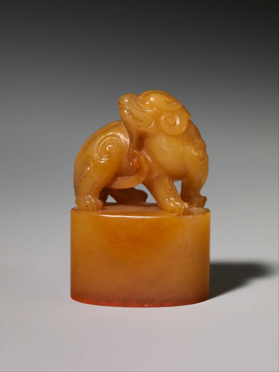 A seal of honey-yellow soapstone; a small lion-like beast crouches on top of the square block.
